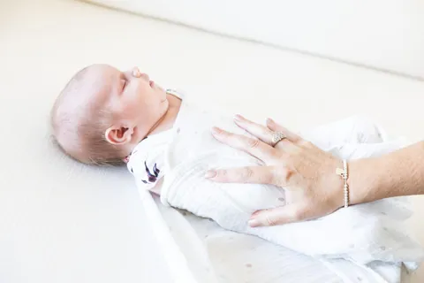 A caregiver's hand resting gently on a swaddled sleeping newborn