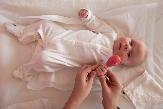 A caregiver's hands holding a small toy for an infant lying on a white blanket