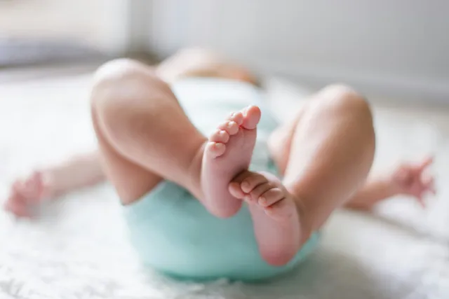 Close-up of a baby's bare feet raised in the air while lying on a soft white rug in a mint onesie